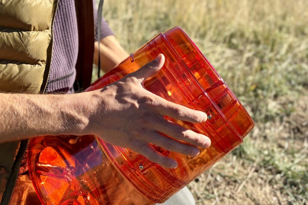 a close up of a hiker pressing the push locks on an orange bear canister