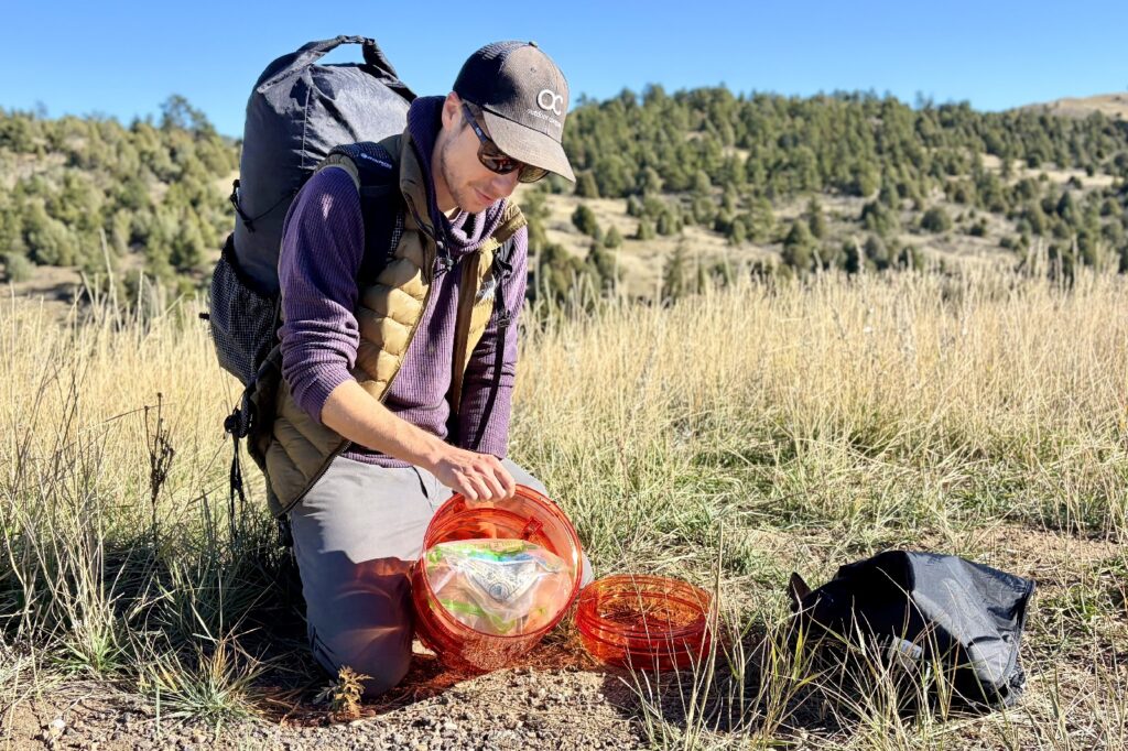 a hiker tips an orange bear canister over to show its inside