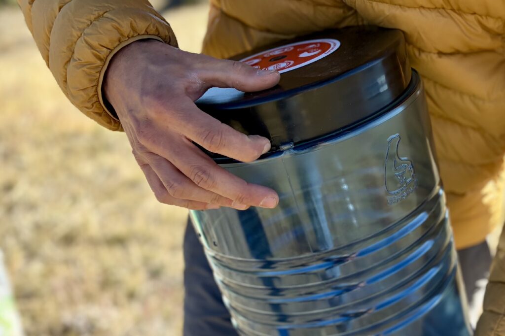 a close up of a a hiker pushing in the locking tab on a bear canister lid