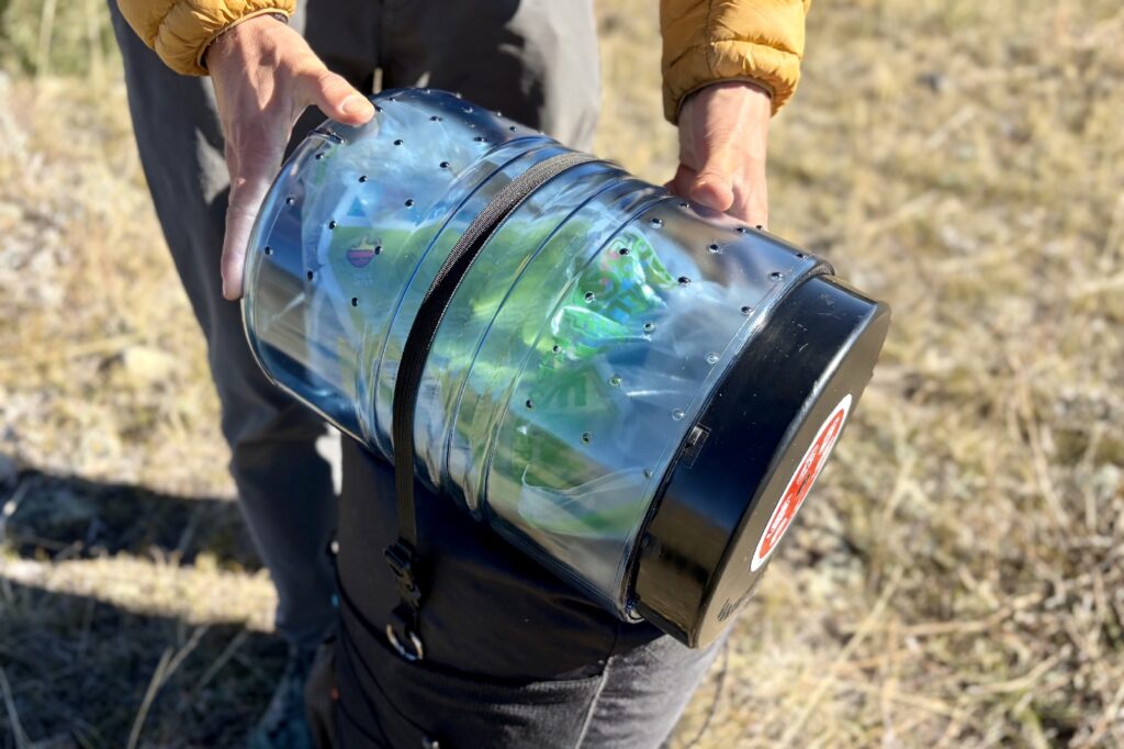 a hiker stabilizes a bear canister packed on a backpack