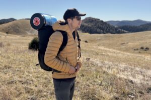 a hiker stands on a trail with a backpack and a blue bear canister strapped on top