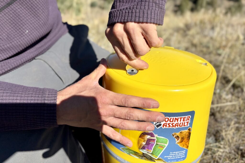 a hiker twists the key lock on a yellow bear canister with the back of a key