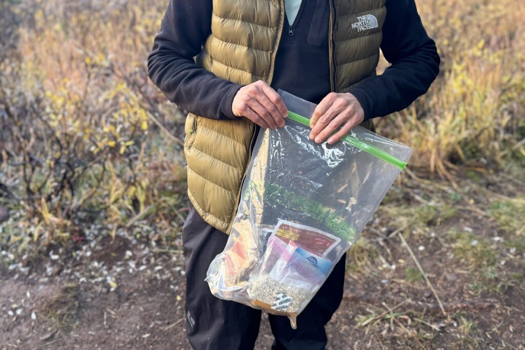 a hiker zips closed a large plastic bag filled with food