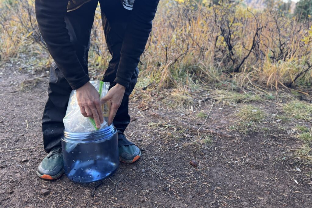 a hiker stuffs a smellyproof bag fool of food into a small bear canister