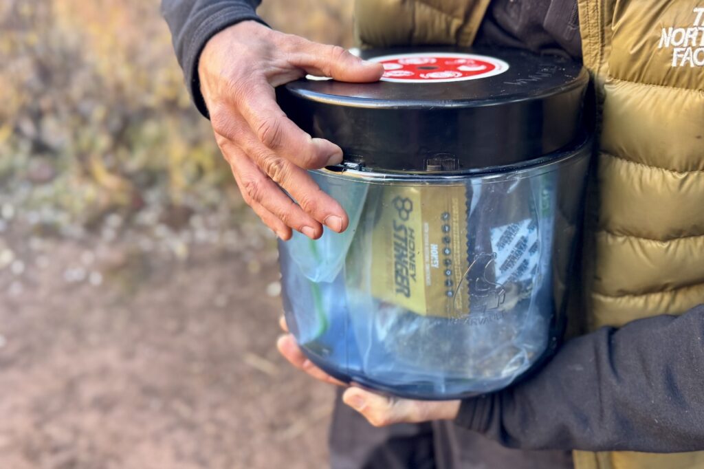 a close up of a hiker pushing the locking tab on the lid of a bear canister