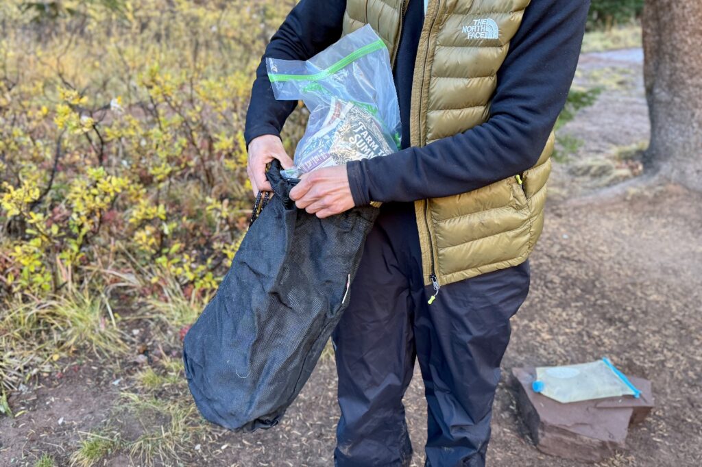 a hiker stuffs a plastic bag full of food into a black drawstring bag