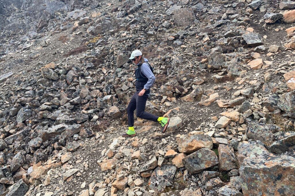 A man runs down a rocky slope wearing green gaiters