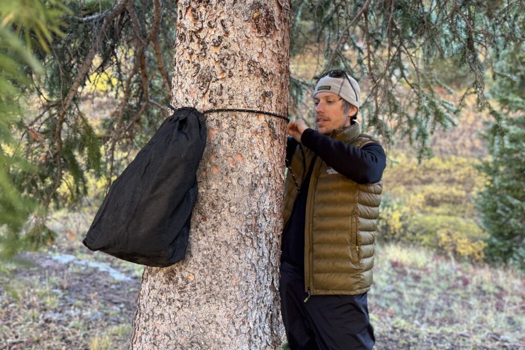 a hiker ties an ursack around a tree trunk