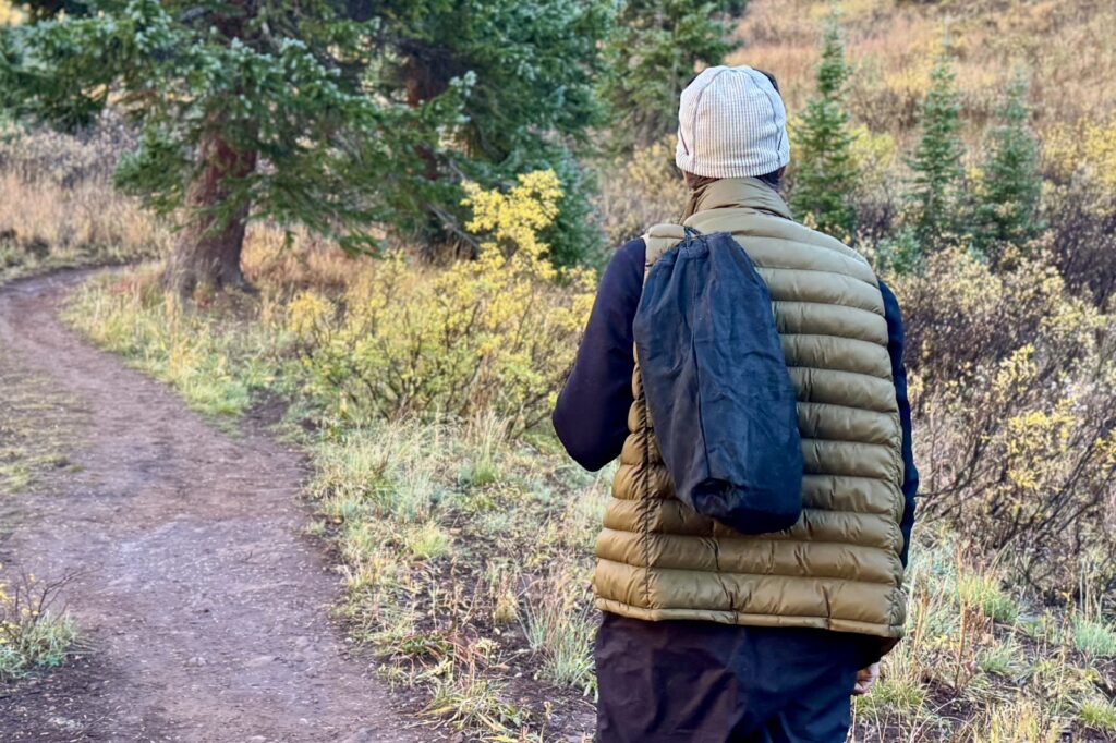 a hiker walks away from the camera with a black drawstring bag slung over his shoulder