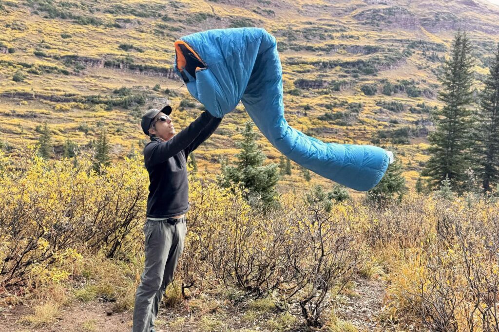 a hiker tosses a blue sleeping bag into the air
