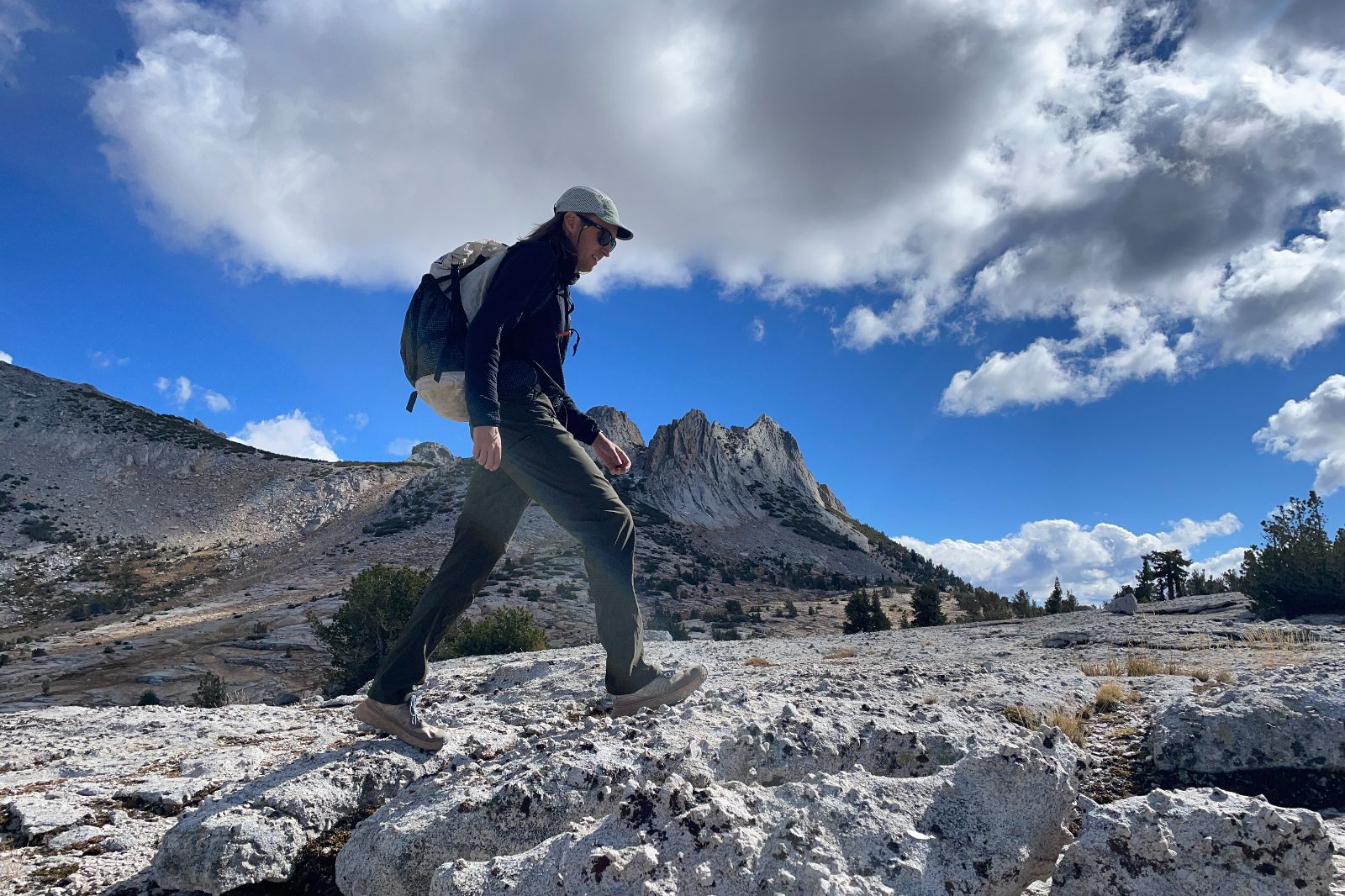 A man walks on a rocky bench in the alpine wearing green pants.