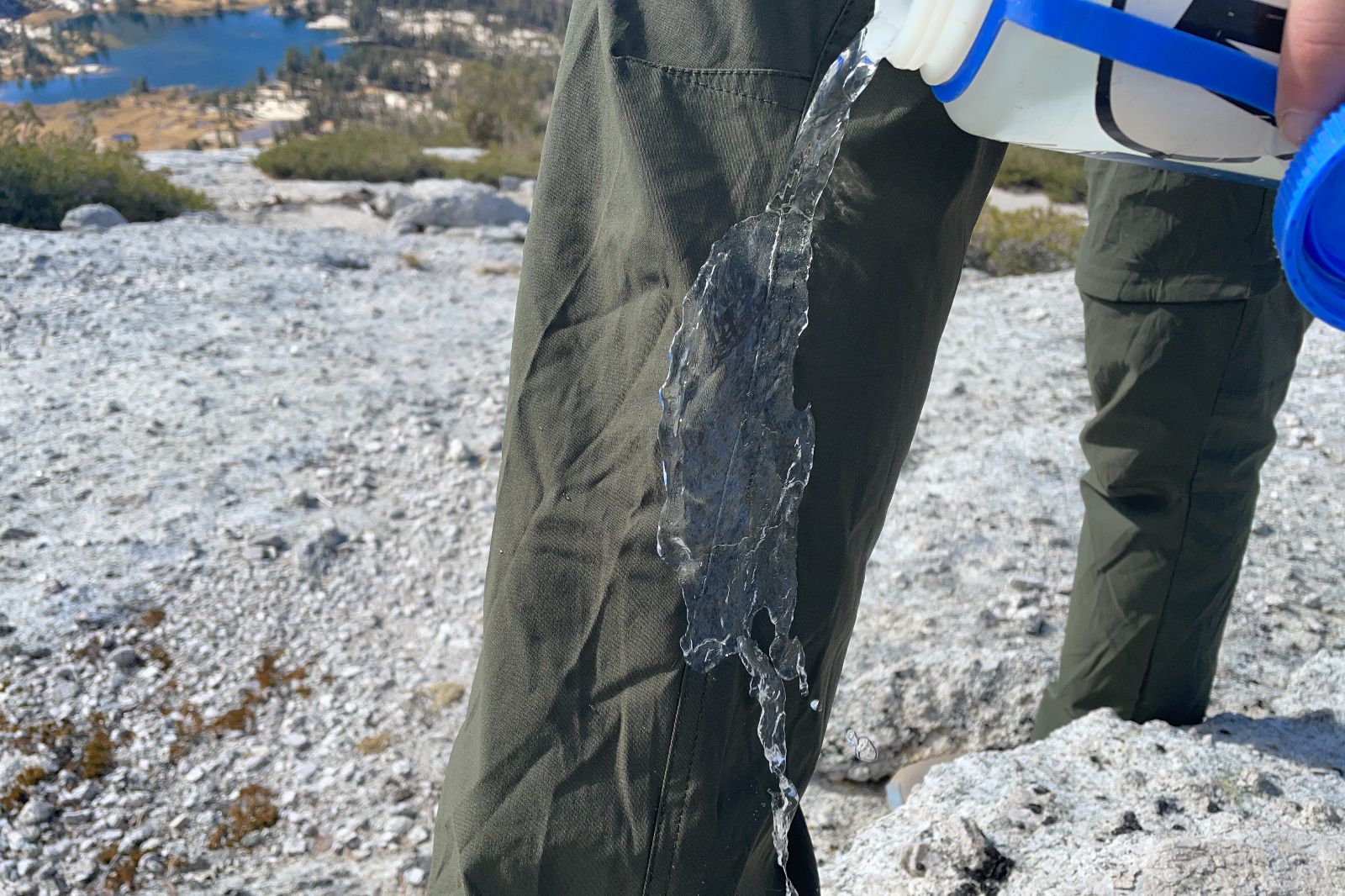 A closeup of water being splashed on the leg of green hiking pants.