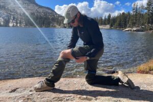 A man converts his convertible pants into shorts alongside a lake.