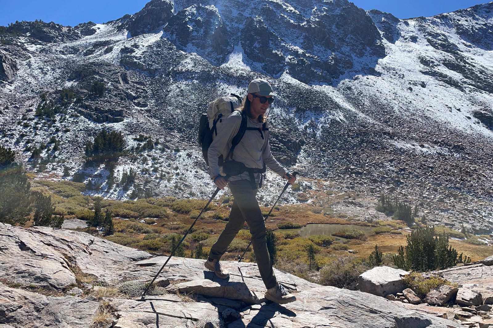 A man hikes down a rock slab with a snowy mountain in the background.
