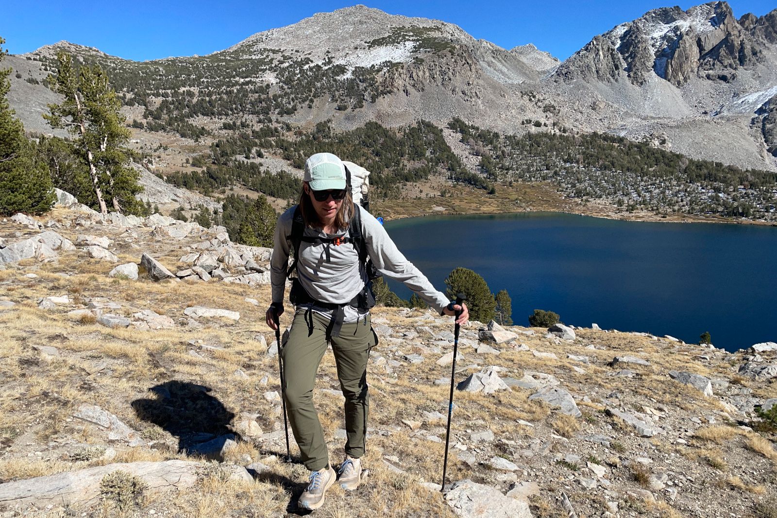 A man hikes above an alpine lake wearing green pants.