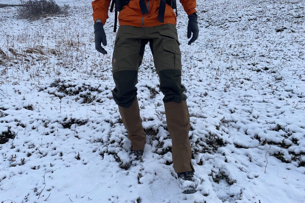 A man walks down a snowy slope while wearing hiking gaiters.