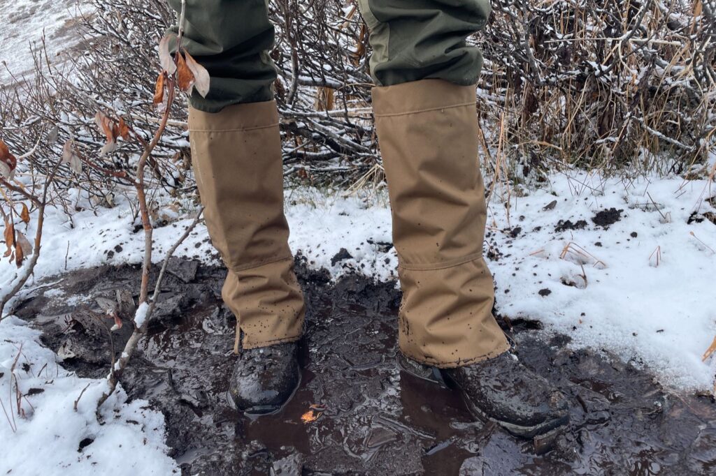 A closeup of a man standing in snow and mud while wearing gaiters.