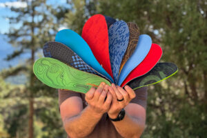Person holding a fan of colorful hiking insoles outdoors with trees in the background.