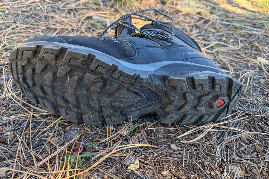 Detailed view of the aggressive tread pattern on the Salomon Quest 4 boot sole with Contagrip branding, resting on forest floor.