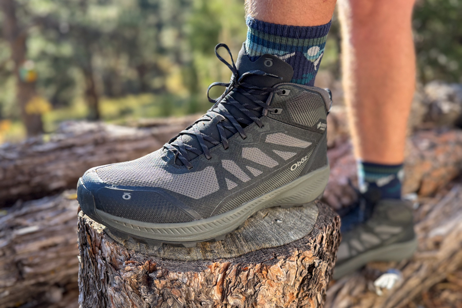 Close-up side view of the Oboz Katabatic LT Mid hiking boot on a tree stump, showing the mesh and synthetic upper design and trail-ready stance.
