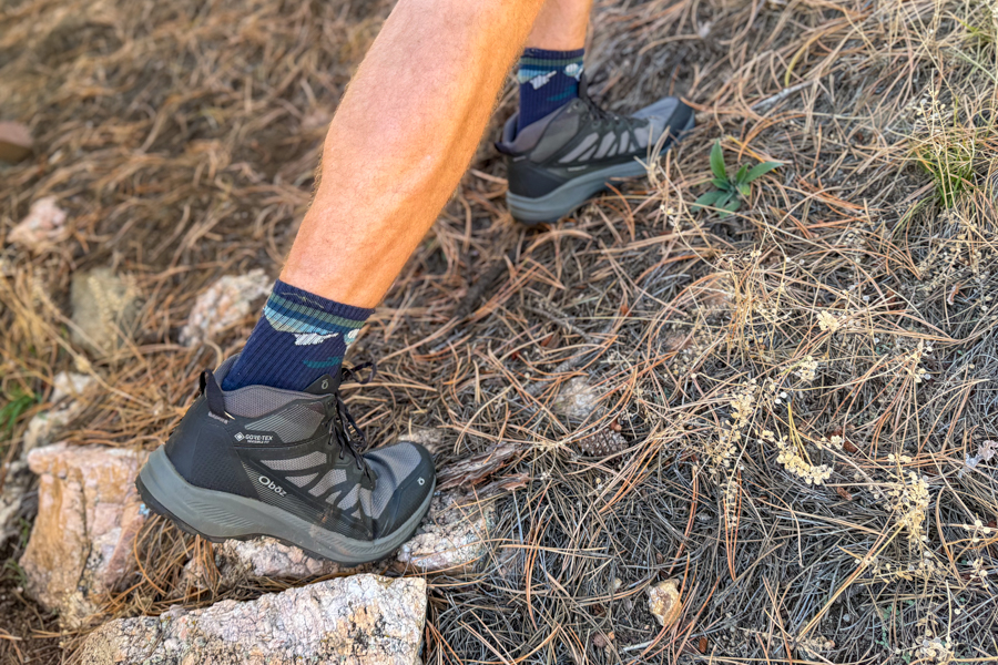 Oboz Katabatic LT Mid boots ascending a pine-covered slope, demonstrating trail performance and ankle support while hiking.