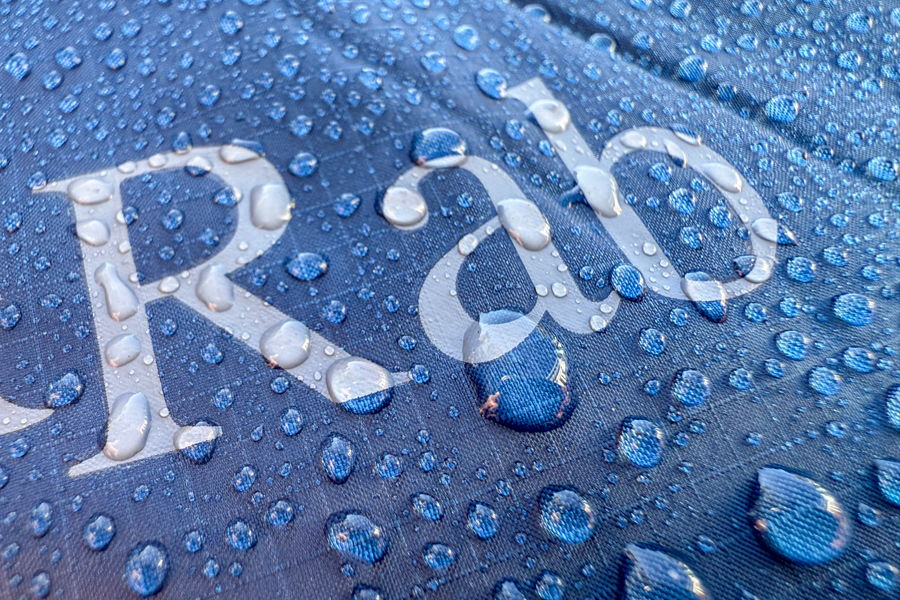 Close-up of the Rab logo on the jacket’s outer shell with water beading across the surface, highlighting the durable water-repellent finish.