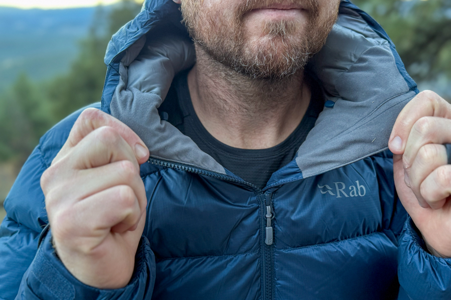 Close-up of the Rab logo on the jacket’s upper chest area with the hood slightly open, highlighting the soft inner collar material.