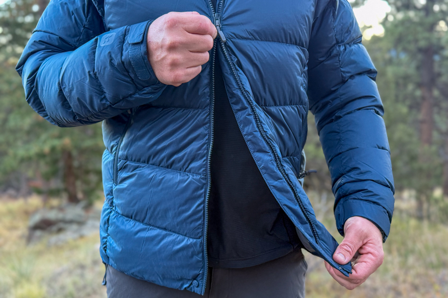 Close-up of a person zipping up the front of the Rab Neutrino Pro, showing the dual zipper design and thick insulation.
