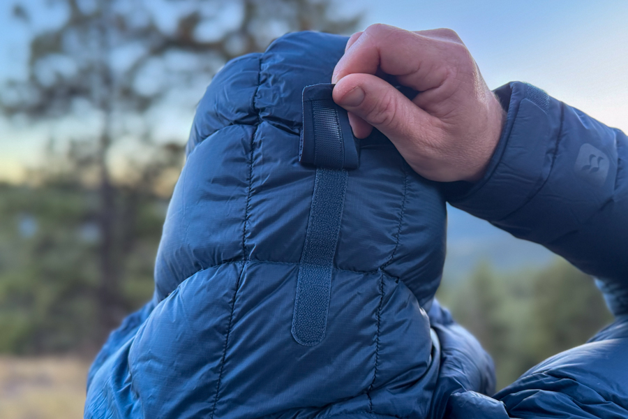 A person adjusts the back cinch tab on the hood of the Rab Neutrino Pro jacket, showing the hood’s adjustability feature.