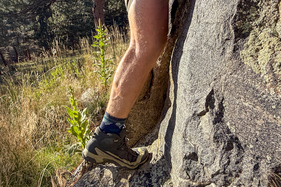 A hiker wearing the Salomon X Ultra 5 Mid GTX boots stands on a rock slab, showcasing the boot’s supportive midsole and heel structure in a steep incline scenario.