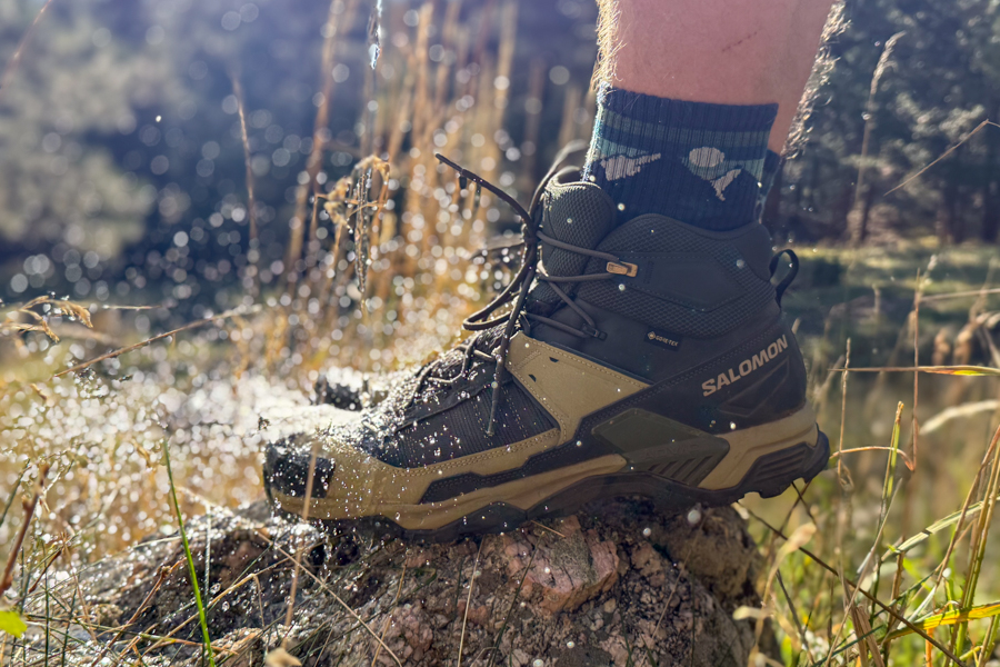 The Salomon X Ultra as water splashes up around it, demonstrating its waterproof GORE-TEX construction in action.