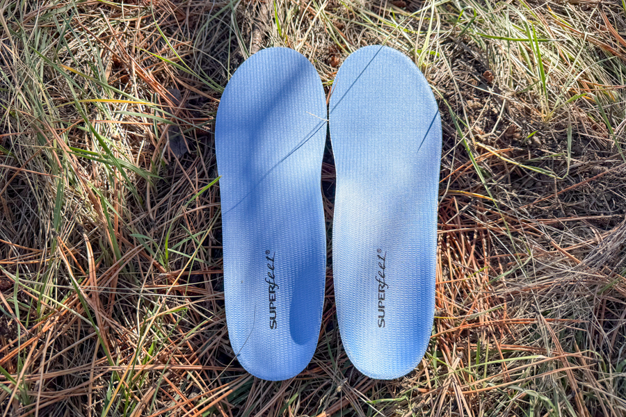 A pair of Superfeet Blue insoles laid side by side on pine needles and grass, showing off their symmetrical build and streamlined shape.