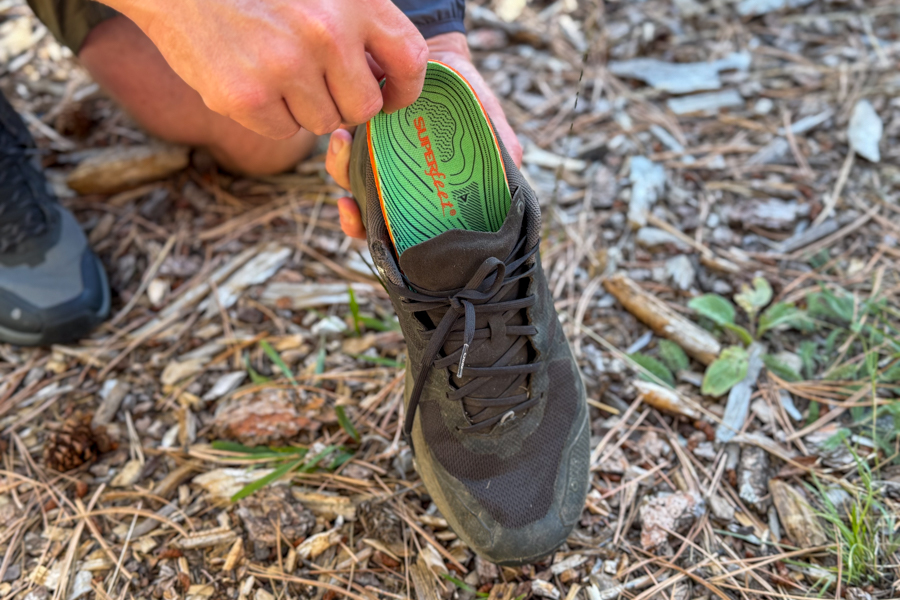 Person inserting a Superfeet Hike Support insole into a black trail shoe in a forested area.