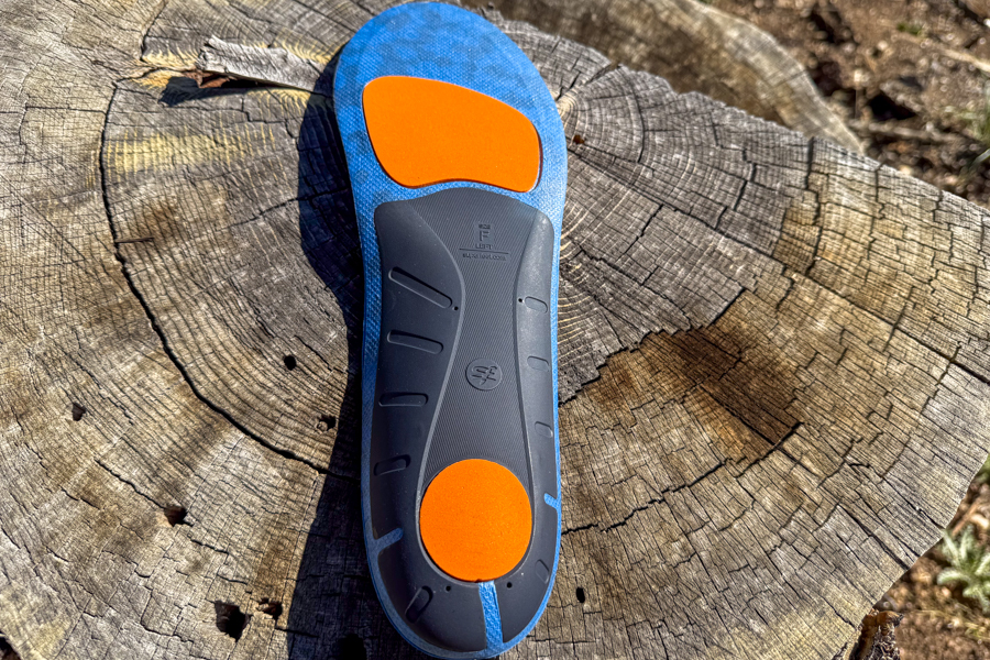 Bottom view of Superfeet Run Cushion insoles resting on a tree stump, showing orange shock-absorbing zones.