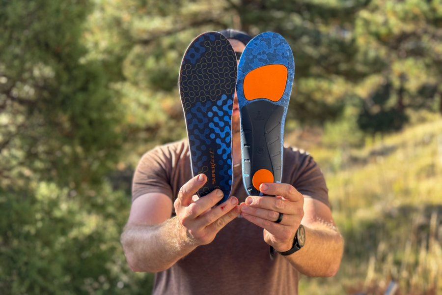 A person holds up both sides of the Superfeet Run Cushion insoles to show the top and bottom details.
