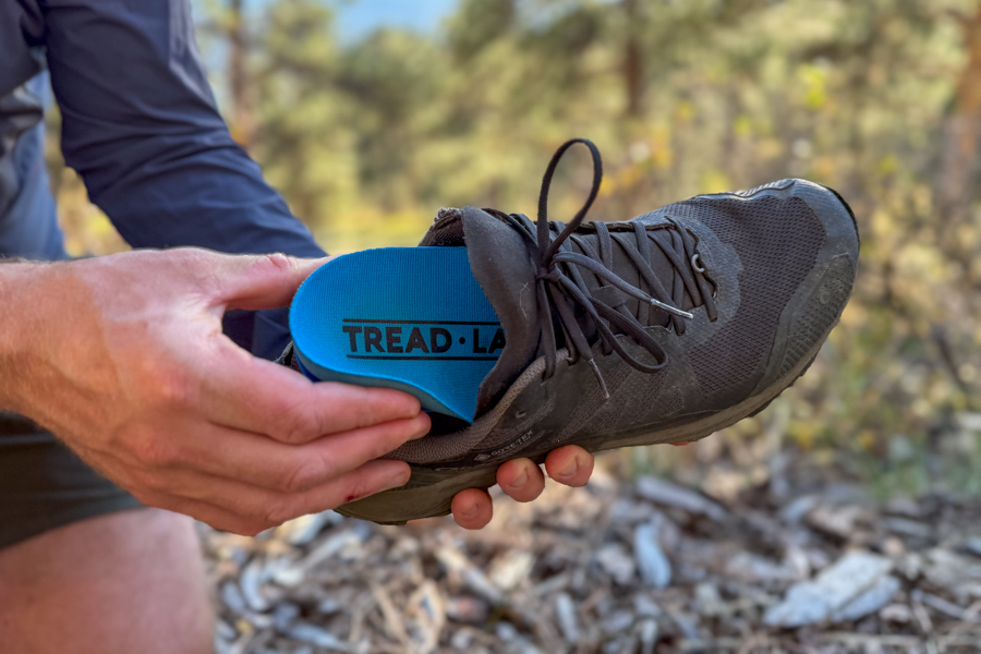 Hand placing a Tread Labs Pace Insole into a trail running shoe, outdoors on a dirt path.