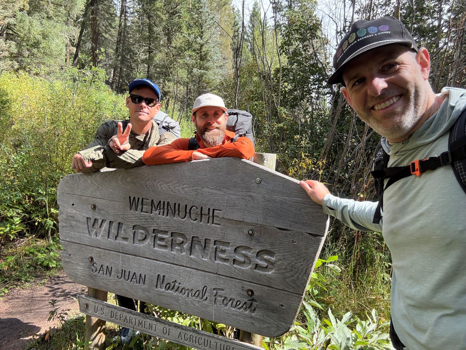 Three male hikes pose for a picture around a Weminuche Wilderness sign in the San Juan National Forest