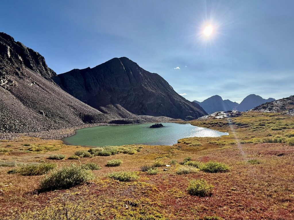 The sun shines brightly on a small mountain lake at the foot of gray mountains at high elevation