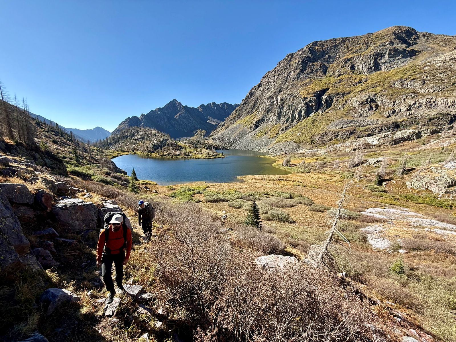 Two male hikers ascend from an alpine lake in the Central San Juan mountains