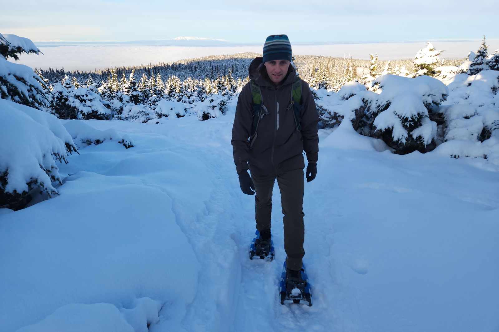 A man walks up a snowy trail wearing snowshoes.