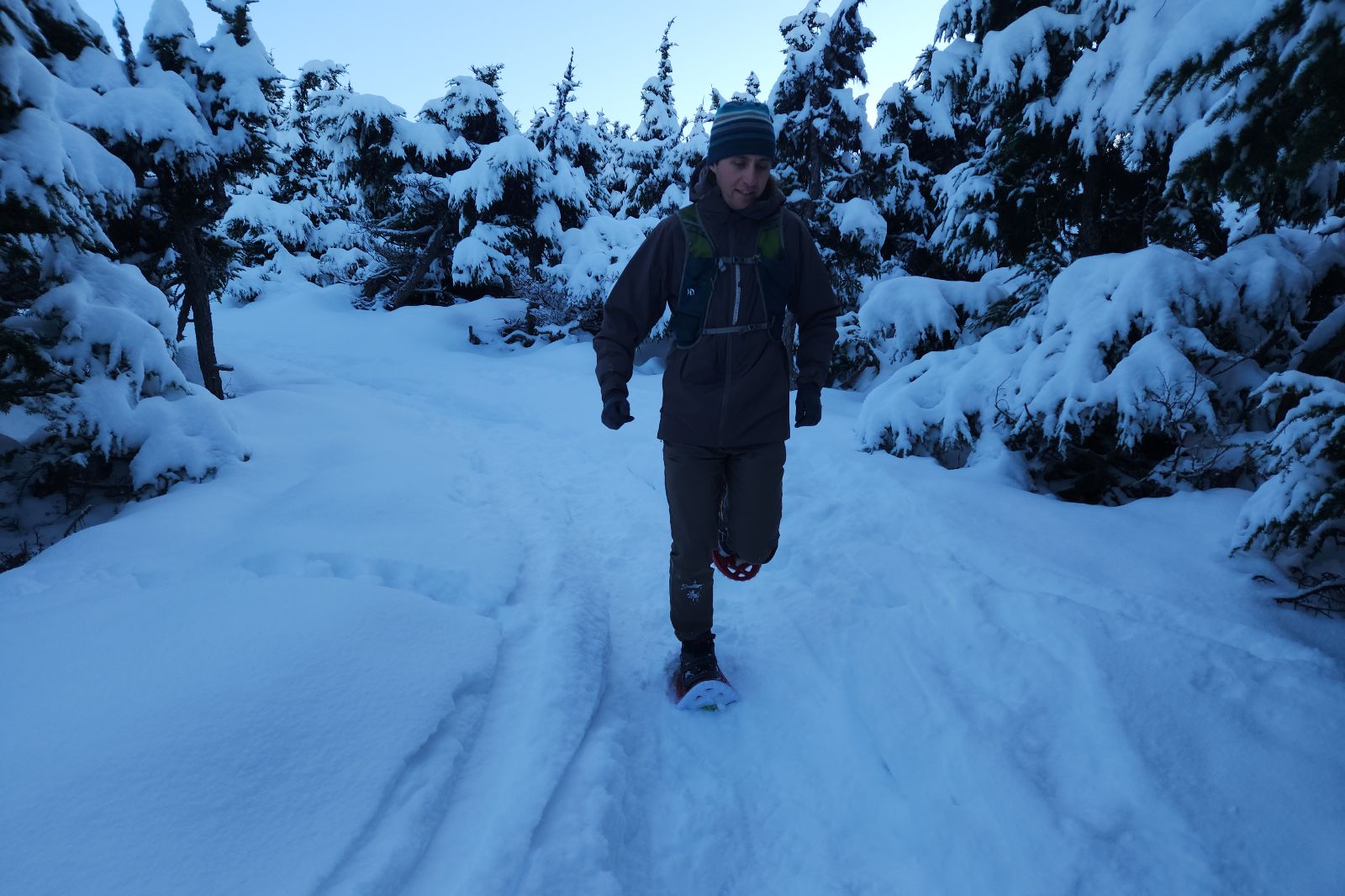 A man runs down a winter trail wearing snowshoes.