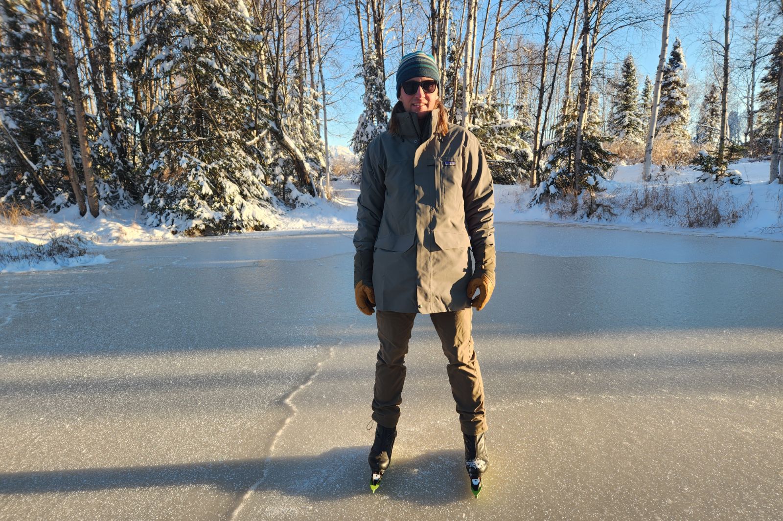 A man stands on the ice in the sun wearing a green jacket.
