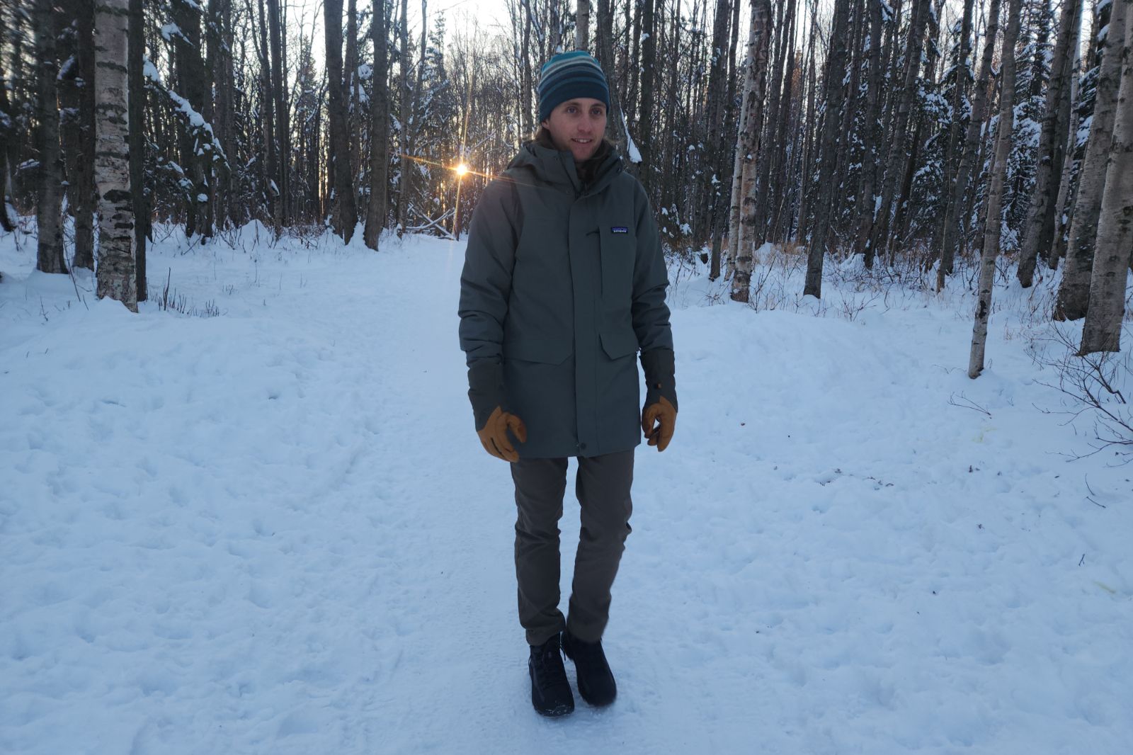A man hikes down a winter trail at sunset.