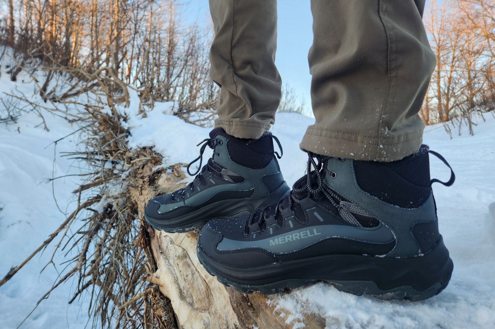 A side view of boots standing on a snow-covered log.