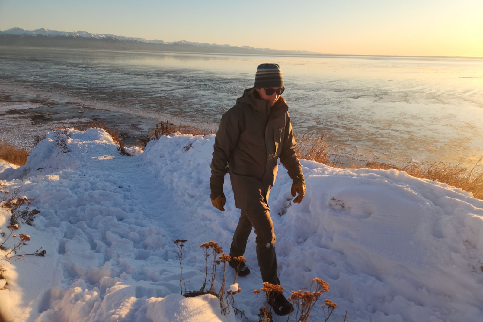 A man hikes up a snowy hill above the ocean.