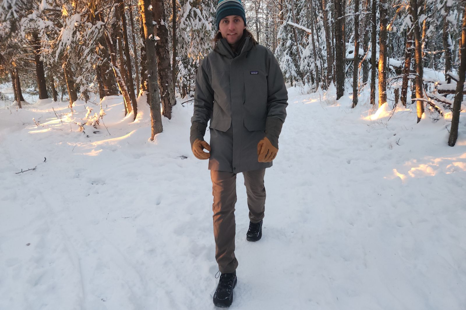 A man walks down a snowy trail wearing a green jacket.
