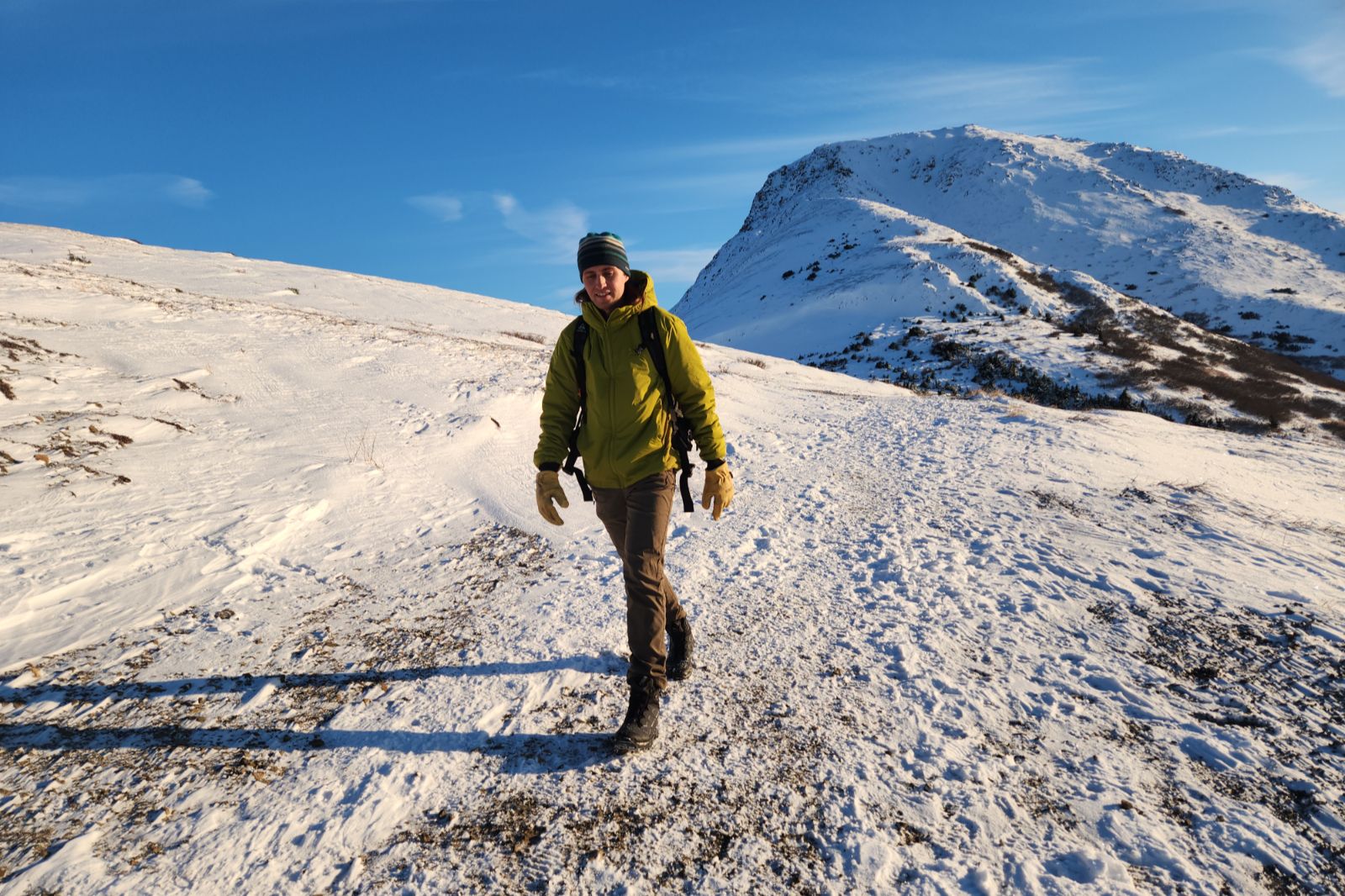 A man walks through the tundra with a mountain in the background.