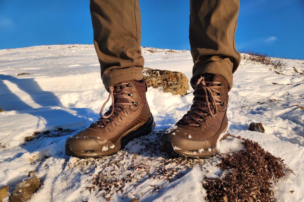 A pair of boots stands on tundra and snow.