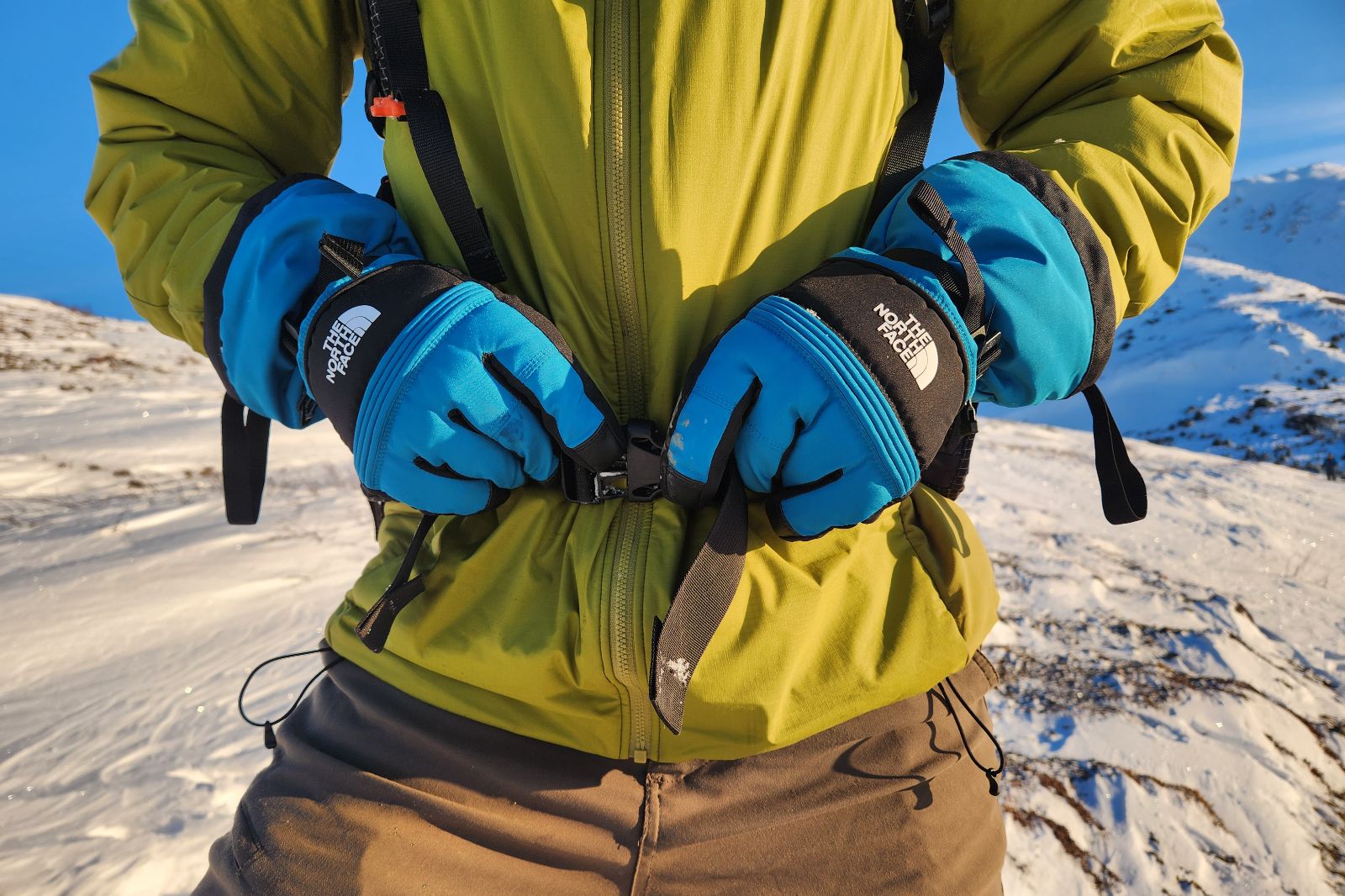 A pair of blue gloves buckles a backpack strap.
