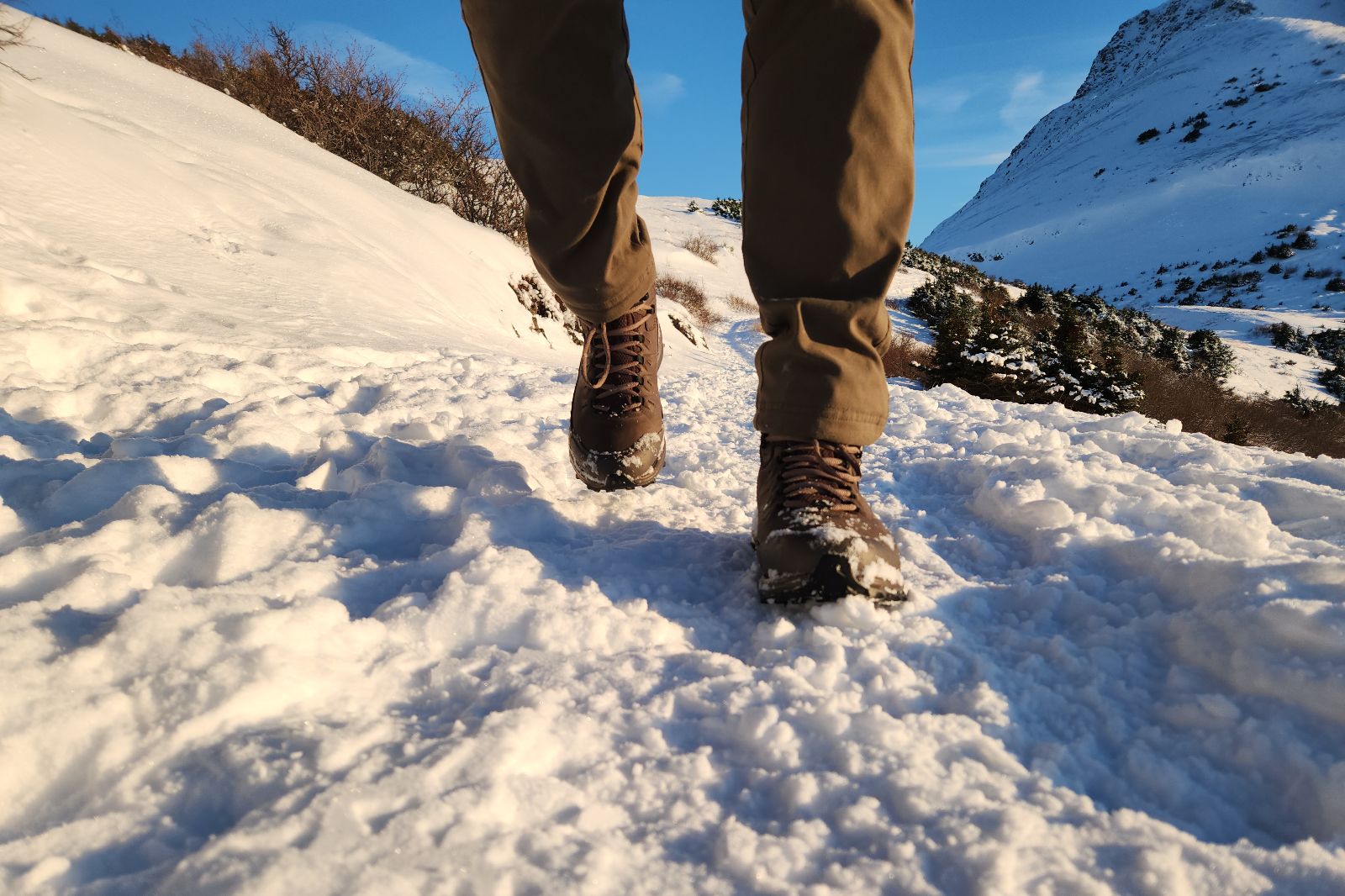 A closeup of boots walking toward the camera on a snowy trail.